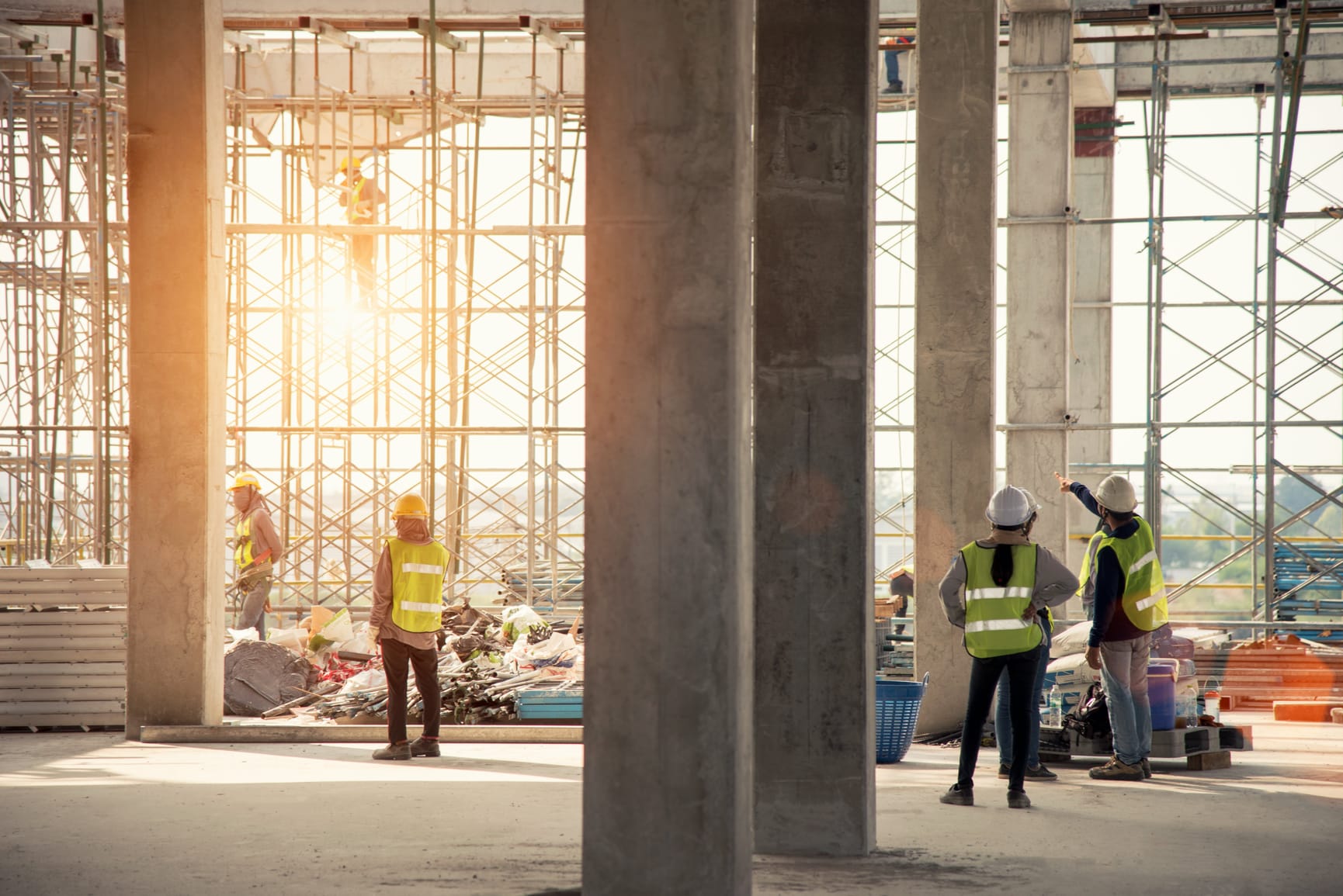 Constructions site with large pillars rising up through centre, with constructions workers in hi-vis.