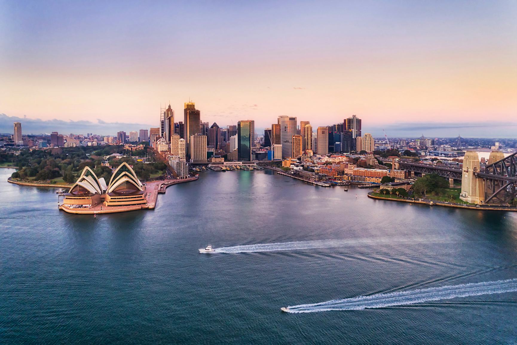 Sydney harbour and skyline captured at sunset with two boats zipping across the water 