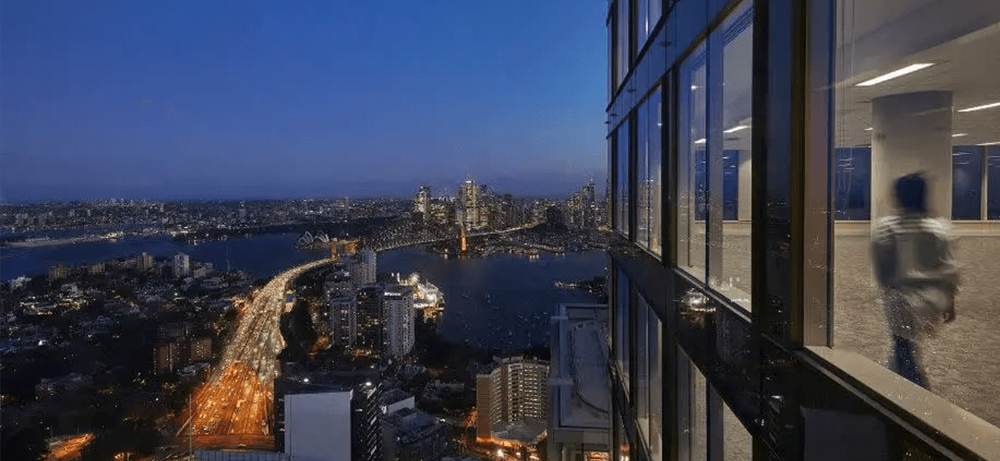 Night time with bridge crossing river and inside view of office building on right.