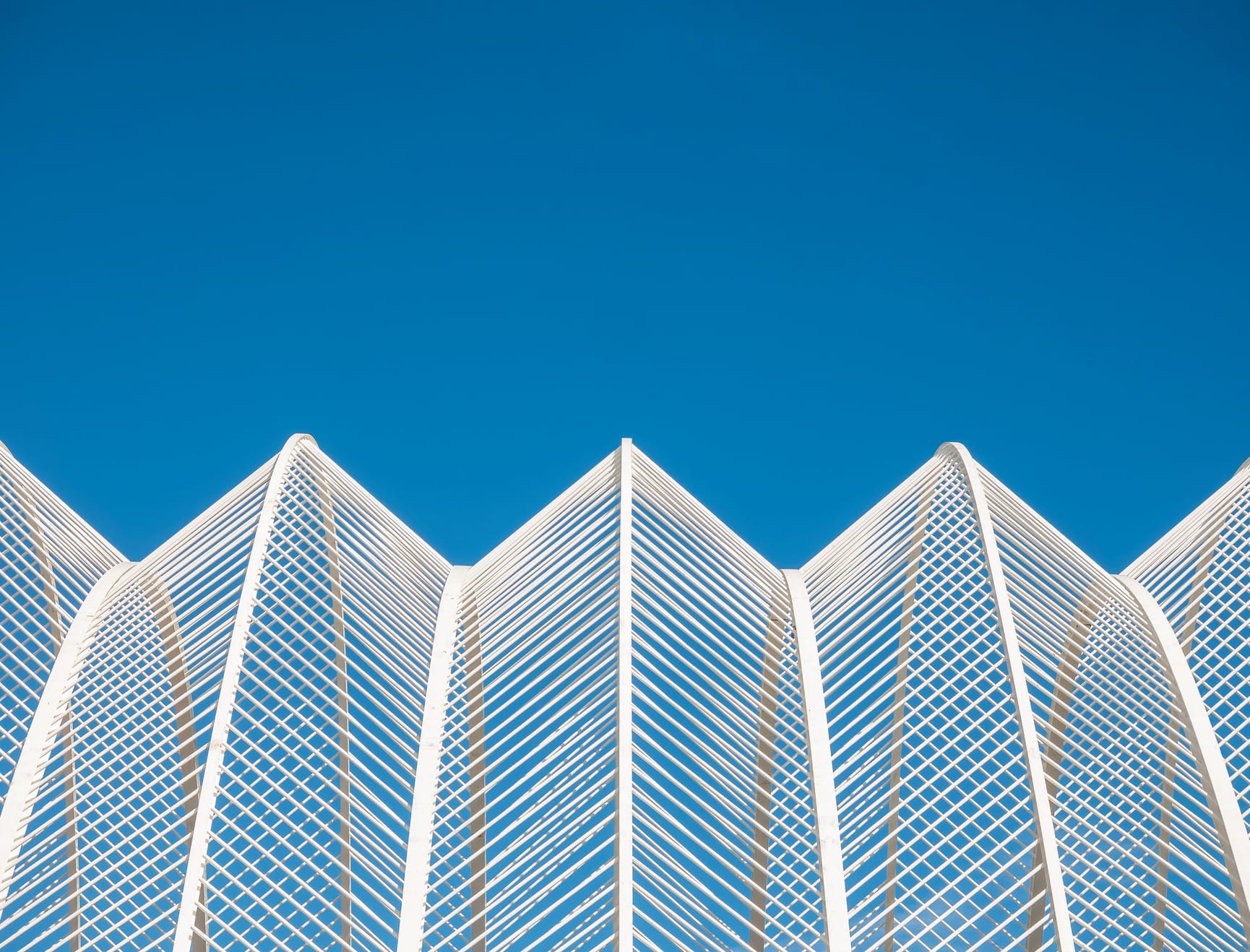 Architectural detail of a metal accordion and lattice shaped building with blue sky visible behind.
